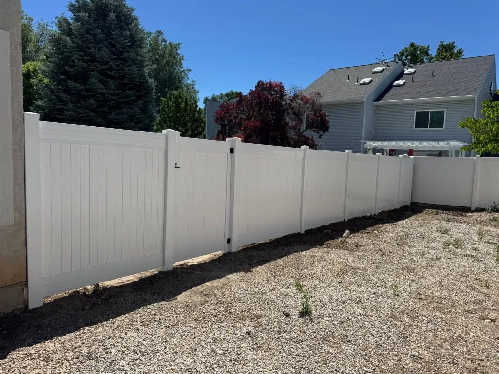 White vinyl privacy fence with a walk gate beside a gravel yard