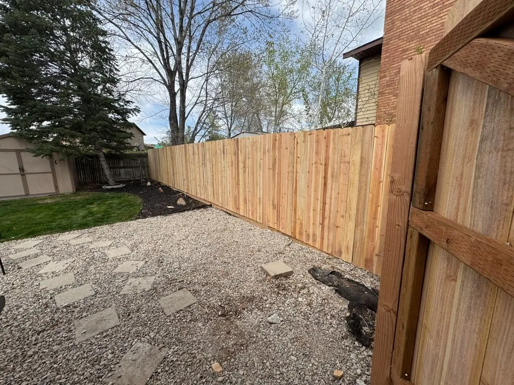New wood privacy fence along a backyard with gravel and stepping stones